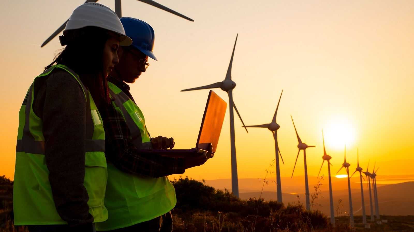 Working people in helmets and reflective vests against the background of windmills