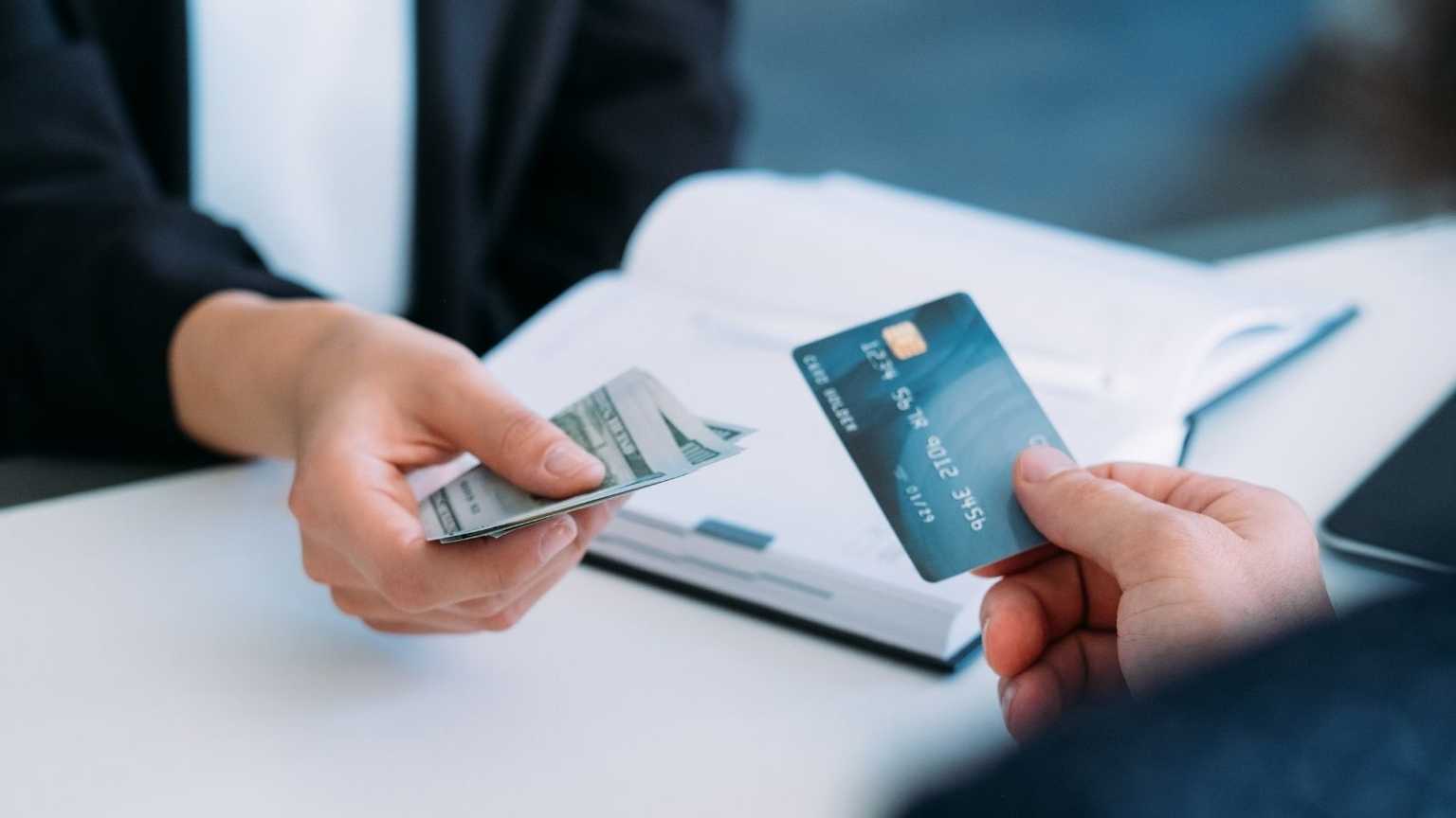 Two people holding cash and a payment card in their hands