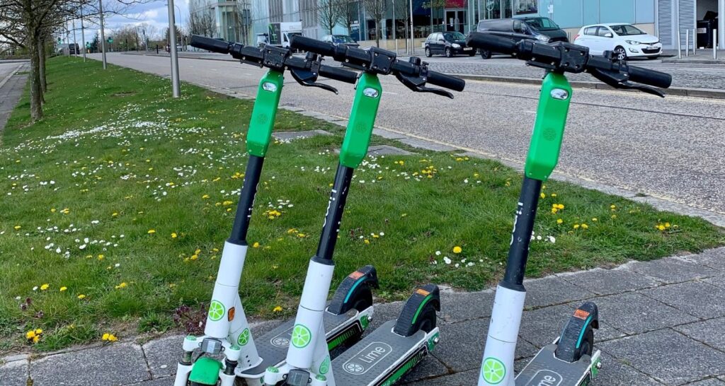 Scooters standing on the pavement next to urban greenery