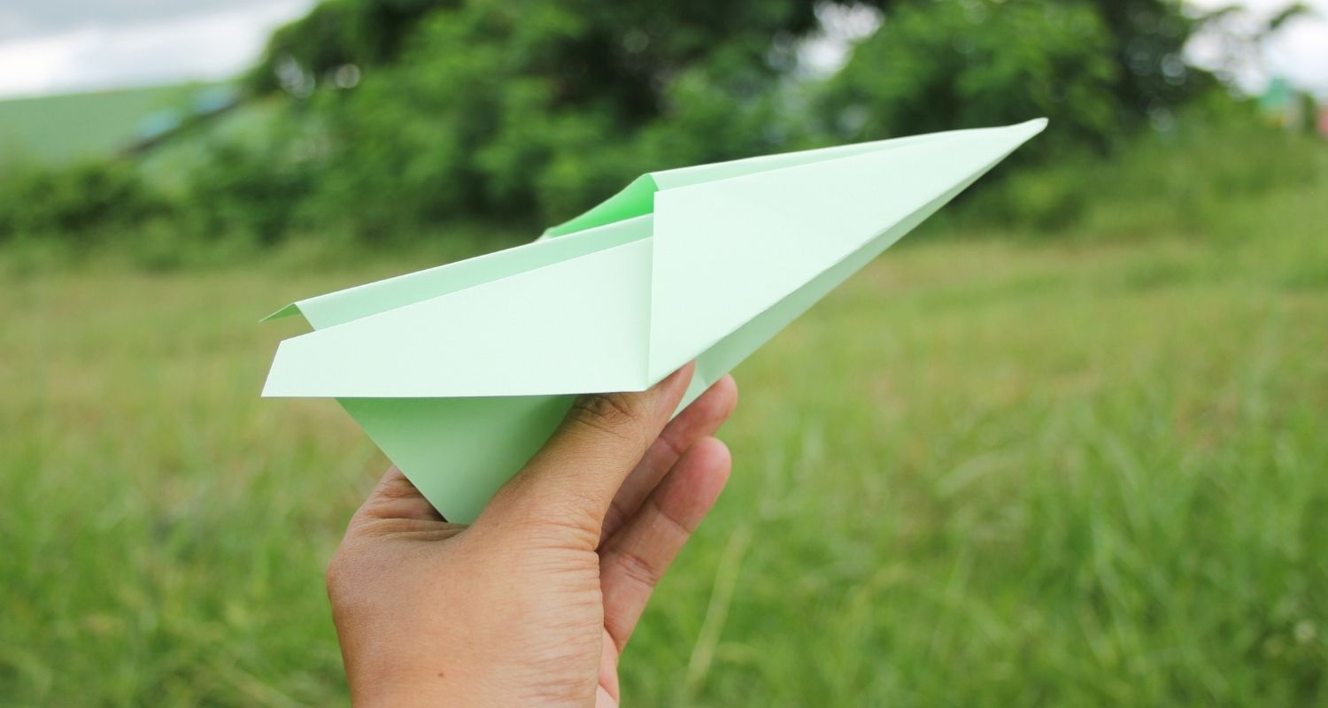 Paper plane held in hand, meadow in the background