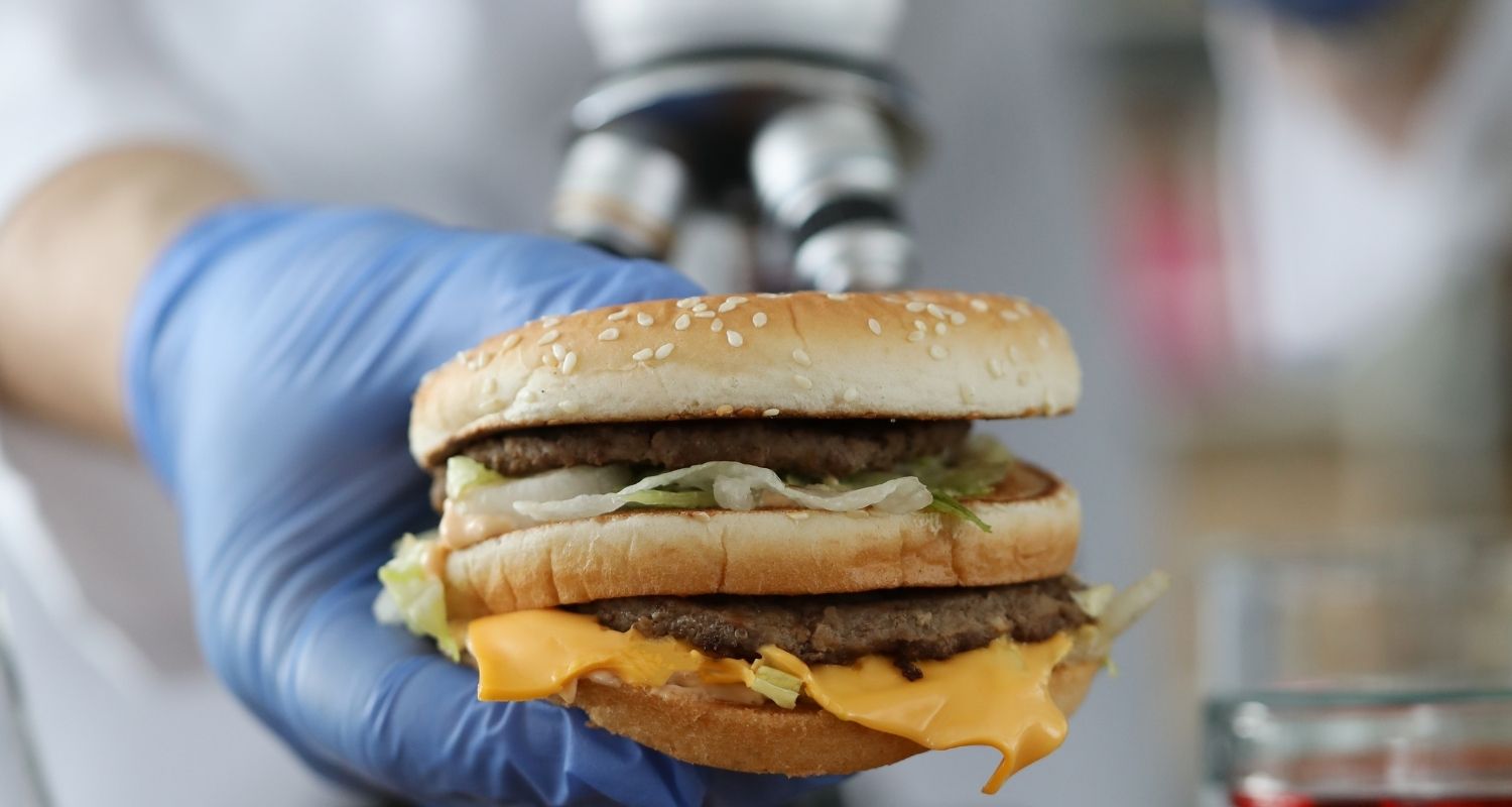 A hand in a disposable glove holds a hamburger